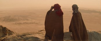 Movie still from “The Mummy” (2017), directed by Alex Kurtzman – A man standing on top of a hill near a body of water; Wide shot, Over the shoulder angle