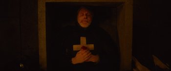 Movie still from “The Mummy” (2017), directed by Alex Kurtzman – A man in a black robe holding a white cross; Medium shot, Overhead angle