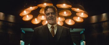 Movie still from “The Mummy” (2017), directed by Alex Kurtzman – A man wearing a suit and tie standing in front of lights; Medium shot, Low angle