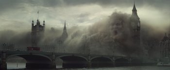 Movie still from “The Mummy” (2017), directed by Alex Kurtzman – Smoke billows from a fire in a building on a bridge over a body of water; Extreme Wide shot, Low angle