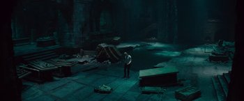 Movie still from “The Mummy” (2017), directed by Alex Kurtzman – A man standing in a dark room with a pool of water; Wide shot, High angle