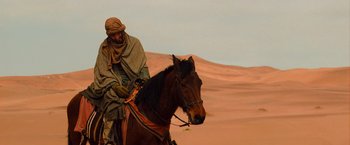 Movie still from “The Mummy” (2017), directed by Alex Kurtzman – A man riding on the back of a brown horse in the desert; Wide shot, Low angle