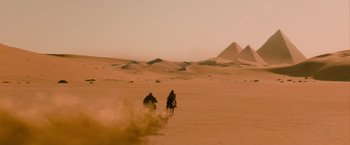 Movie still from “The Mummy” (2017), directed by Alex Kurtzman – Two people riding horses in the desert near some sand dunes; Extreme Wide shot, High angle