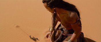 Movie still from “The Mummy Returns” (2001), directed by Stephen Sommers – A man in native dress looking at a scorpion; Medium shot, High angle