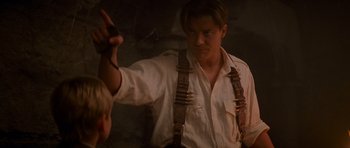 Movie still from “The Mummy Returns” (2001), directed by Stephen Sommers – A man in white shirt and brown suspenders holding a gun; Medium shot, Over the shoulder angle