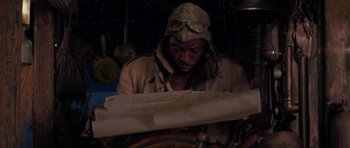 Movie still from “The Mummy Returns” (2001), directed by Stephen Sommers – A man wearing a hat and jacket looking at a paper; Medium shot, High angle