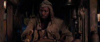 Movie still from “The Mummy Returns” (2001), directed by Stephen Sommers – A man wearing a hat and holding a steering wheel in a dark room; Close Up shot, High angle