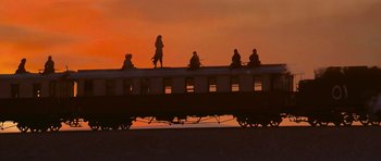 Movie still from “The Mummy Returns” (2001), directed by Stephen Sommers – People sitting on top of a passenger train at sunset; Extreme Wide shot, Low angle