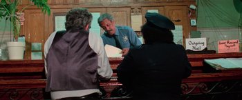 Movie still from “The New York Ripper” (1982), directed by Lucio Fulci – A man in a police uniform sitting in front of two other men; Medium shot, Low angle