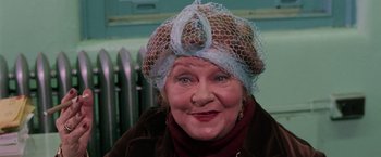 Movie still from “The New York Ripper” (1982), directed by Lucio Fulci – An older woman wearing a hat and smiling; Close Up shot, Over the shoulder angle