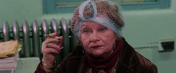 Movie still from “The New York Ripper” (1982), directed by Lucio Fulci – An older woman wearing a blue veil and a brown jacket; Close Up shot, High angle