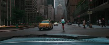 Movie still from “The New York Ripper” (1982), directed by Lucio Fulci – A woman riding a bike down a street past a yellow taxi cab; Extreme Wide shot, Over the shoulder angle