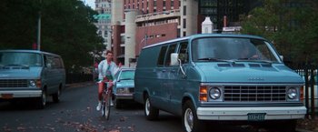 Movie still from “The New York Ripper” (1982), directed by Lucio Fulci – A man riding a bike down a street next to a van; Wide shot, Low angle