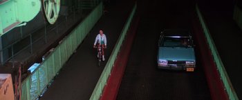 Movie still from “The New York Ripper” (1982), directed by Lucio Fulci – A man riding a bike down a street at night; Extreme Wide shot, Overhead angle