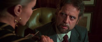 Movie still from “The New York Ripper” (1982), directed by Lucio Fulci – A man wearing a suit and tie holding a pair of scissors in his hand; Close Up shot, Over the shoulder angle