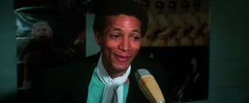Movie still from “The New York Ripper” (1982), directed by Lucio Fulci – A man in a green jacket and a tie is holding a microphone; Close Up shot, Low angle
