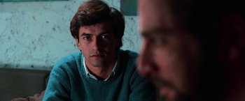 Movie still from “The New York Ripper” (1982), directed by Lucio Fulci – A man sitting in front of another man in front of a wall; Close Up shot, Over the shoulder angle