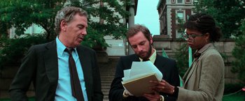 Movie still from “The New York Ripper” (1982), directed by Lucio Fulci – Two men in suits looking at papers in a folder; Medium shot, Over the shoulder angle