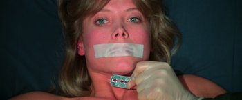 Movie still from “The New York Ripper” (1982), directed by Lucio Fulci – A woman with tape over her mouth holding a razor blade; Close Up shot, Low angle