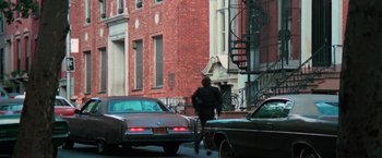 Movie still from “The New York Ripper” (1982), directed by Lucio Fulci – A man walking down a street past a red brick building; Wide shot, Over the shoulder angle