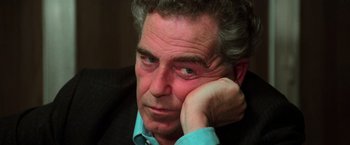 Movie still from “The New York Ripper” (1982), directed by Lucio Fulci – An older man sitting with his head resting on his hand; Close Up shot, High angle