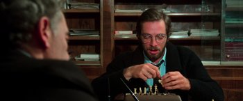 Movie still from “The New York Ripper” (1982), directed by Lucio Fulci – A man sitting at a table playing a game of chess; Close Up shot, Over the shoulder angle