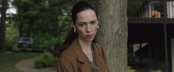 Movie still from “The Night House” (2020), directed by David Bruckner – A woman in a brown jacket standing in front of a tree; Close Up shot, High angle