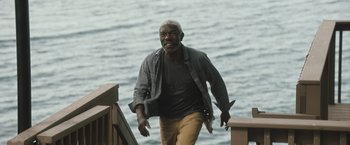 Movie still from “The Night House” (2020), directed by David Bruckner – An older man walking on a bridge near the water; Medium shot, Low angle