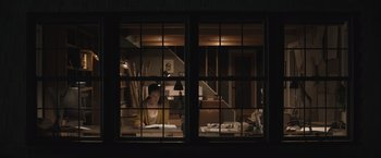 Movie still from “The Night House” (2020), directed by David Bruckner – A woman sitting at a desk in a room with a window open; Wide shot, Low angle