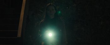 Movie still from “The Night House” (2020), directed by David Bruckner – A woman is holding a flashlight in the dark; Medium shot, Low angle
