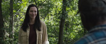 Movie still from “The Night House” (2020), directed by David Bruckner – A woman standing in front of a tree smiling for the camera; Medium shot, Over the shoulder angle