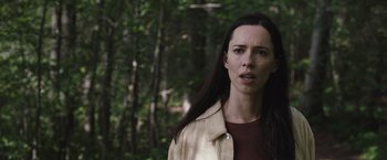 Movie still from “The Night House” (2020), directed by David Bruckner – A woman standing in the woods with trees in the background; Close Up shot, Low angle