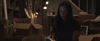 Movie still from “The Night House” (2020), directed by David Bruckner – A woman is reading a book in a dark room; Medium shot, Low angle