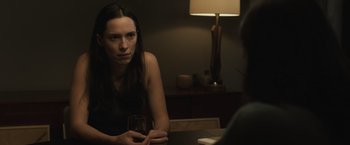 Movie still from “The Night House” (2020), directed by David Bruckner – A woman sitting at a table holding a glass; Close Up shot, Over the shoulder angle