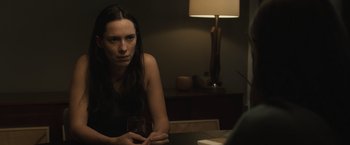 Movie still from “The Night House” (2020), directed by David Bruckner – A woman sitting at a table with a drink in her hand; Close Up shot, Over the shoulder angle