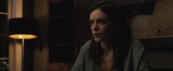 Movie still from “The Night House” (2020), directed by David Bruckner – A woman sitting in front of a book shelf looking at the camera; Close Up shot, Low angle