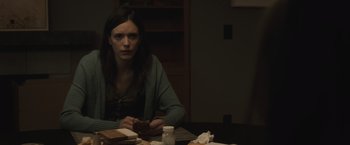 Movie still from “The Night House” (2020), directed by David Bruckner – A woman sitting at a table holding a cell phone; Medium shot, Over the shoulder angle