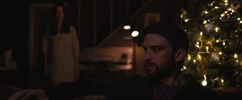 Movie still from “The Night House” (2020), directed by David Bruckner – A man sitting on a couch in a dark room; Medium shot, Over the shoulder angle