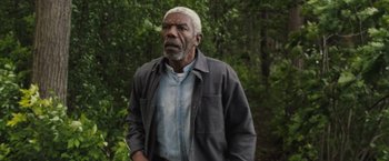 Movie still from “The Night House” (2020), directed by David Bruckner – An older man standing in a wooded area; Medium shot, Low angle