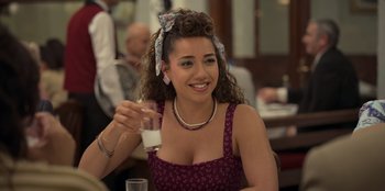 Movie still from “The Nightingale of Bursa” (2023), directed by Hakan Algül – A beautiful young lady sitting at a table holding a glass of milk; Close Up shot, Over the shoulder angle