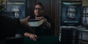 Movie still from “The Noel Diary” (2022), directed by Charles Shyer – A man in glasses is holding a book; Medium shot, Over the shoulder angle
