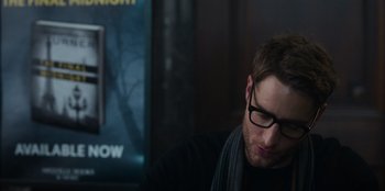 Movie still from “The Noel Diary” (2022), directed by Charles Shyer – A man wearing glasses sitting in front of a movie poster; Close Up shot, Over the shoulder angle