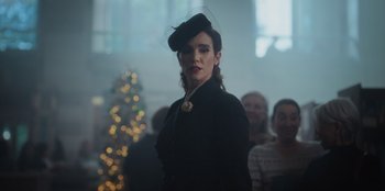 Movie still from “The Noel Diary” (2022), directed by Charles Shyer – A woman wearing a black hat standing in front of a group of people; Close Up shot, Over the shoulder angle