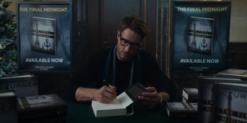 Movie still from “The Noel Diary” (2022), directed by Charles Shyer – A man writing on a book while sitting at a table; Medium shot, High angle