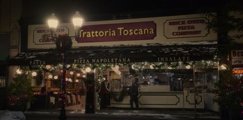 Movie still from “The Noel Diary” (2022), directed by Charles Shyer – A man walking in front of a pizza restaurant; Extreme Wide shot, High angle