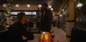 Movie still from “The Noel Diary” (2022), directed by Charles Shyer – A man standing at a table with a glass of red wine; Medium shot, Over the shoulder angle