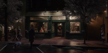 Movie still from “The Noel Diary” (2022), directed by Charles Shyer – A person walks down the sidewalk in front of a store; Extreme Wide shot, Over the shoulder angle