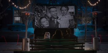 Movie still from “The Noel Diary” (2022), directed by Charles Shyer – People sitting in front of a large screen with a picture of a man and a woman; Wide shot, High angle