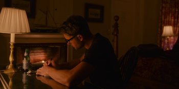 Movie still from “The Noel Diary” (2022), directed by Charles Shyer – A man sitting at a table writing on a piece of paper; Medium shot, Over the shoulder angle