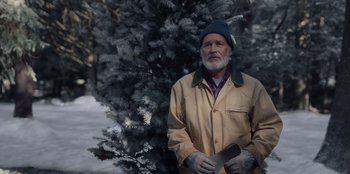Movie still from “The Noel Diary” (2022), directed by Charles Shyer – An older man holding a knife in front of a tree; Medium shot, Over the shoulder angle
